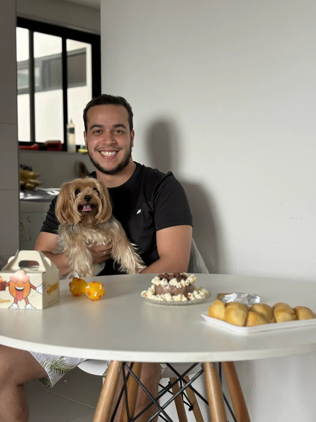 Tarcio em casa, à mesa, com o cachorro no colo